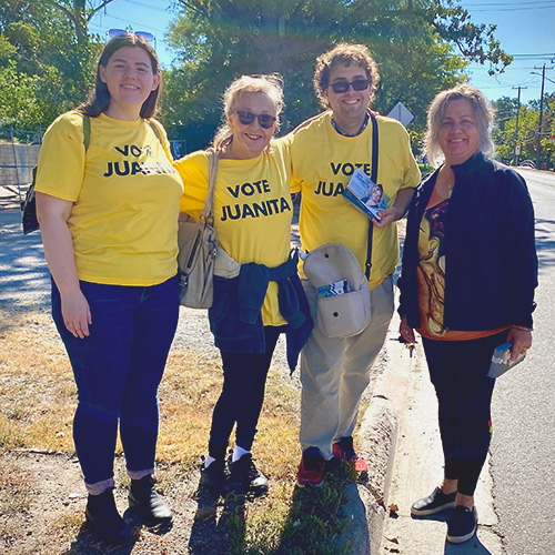 Juanita with 3 campaign volunteers with wearing yellow t-shirts that say Vote Juanita. Standing outdoor with arms around each other.